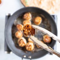 a tong flipping a golden scallop after pan searing