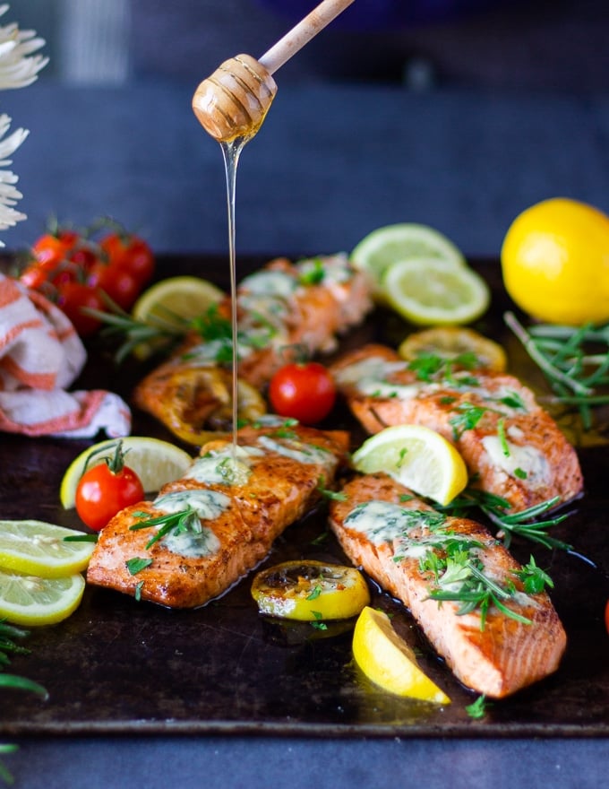 pan seared salmon with blue cheese and a hand drizzling honey on a tray.