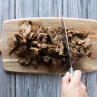 A hand slicing the cooked fajita meat over a wooden board into thinner strips for the fajita recipe