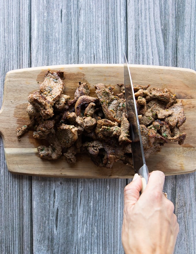 A hand slicing the cooked fajita meat over a wooden board into thinner strips for the fajita recipe