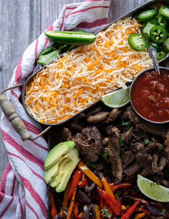 a huge tray of shredded cheese on the sheet pan served next to sheet pan fajitas 