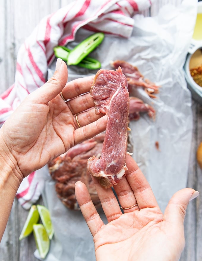 A hand holding sliced pieces of meat showing the size of thickness