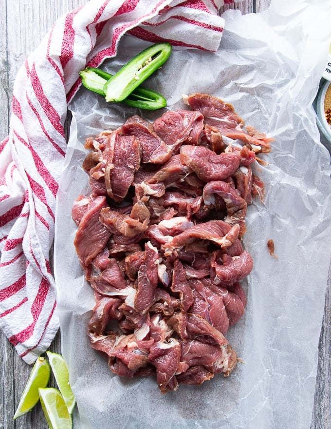 thinly sliced pieces of the meat leg of lamb on a paper lined cutting board ready for marinade