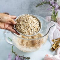 a hand pouring in lots of oats to the bowl of oatmeal cookies