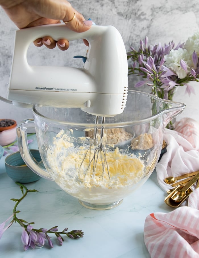 a hand mixer beating up the butter and sugar in a glass bowl to make oatmeal cookies