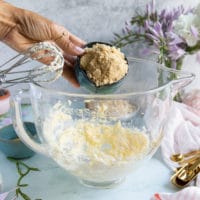 a hand adding in brown sugar to the butter bowl