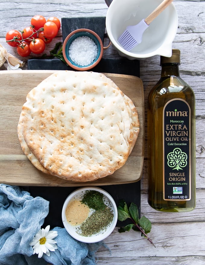 Thick Greek pita bread on a wooden board to be cut up into pita chips