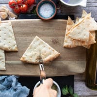 A hand holding a pizza cutter and slicing the quarter of pita bread into two perfect wedges