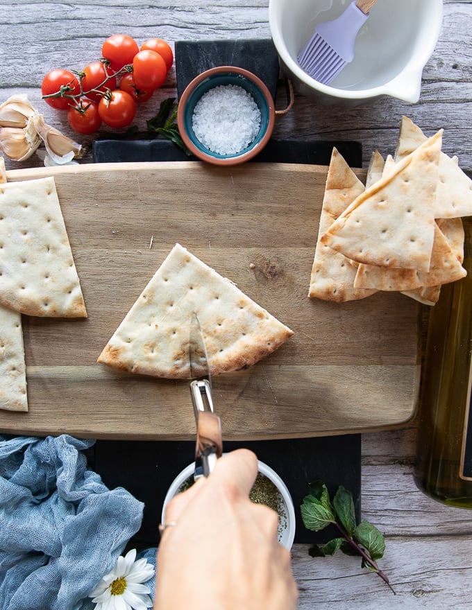 A hand holding a pizza cutter and slicing the quarter of pita bread into two perfect wedges