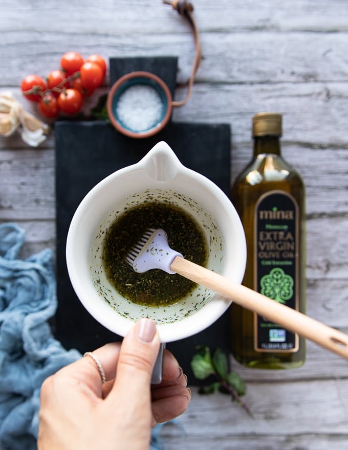 A hand holding a bowl of the spice and olive oil mixture ready to brush the pita chips