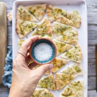 A hand holding a small bowl of coarse salt to be sprinkled over the pita chips before baking