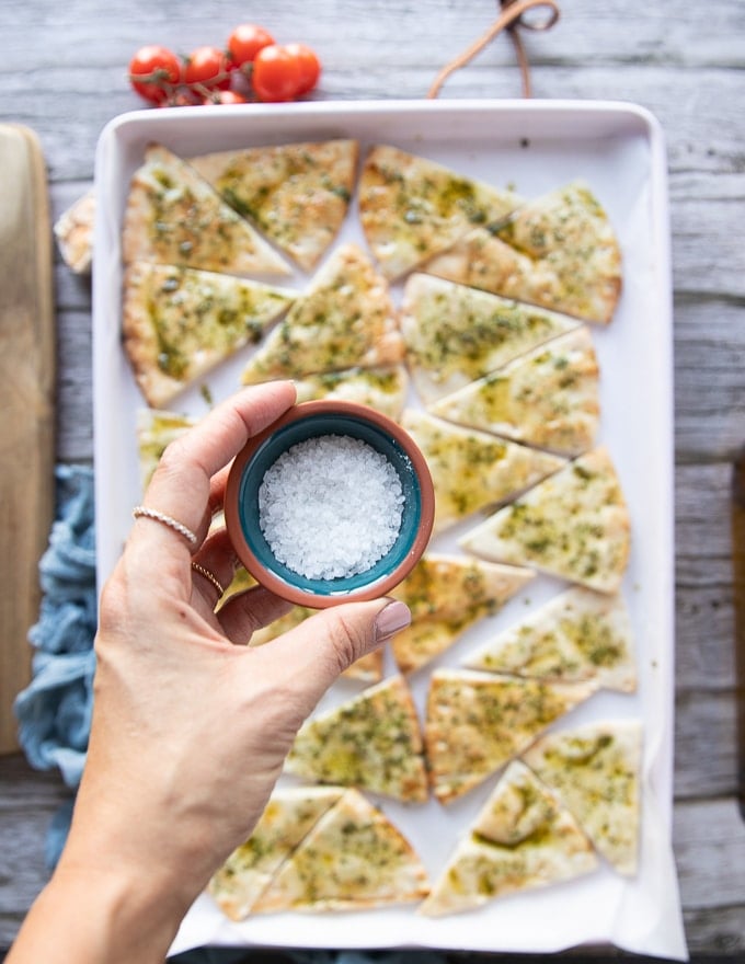 A hand holding a small bowl of coarse salt to be sprinkled over the pita chips before baking