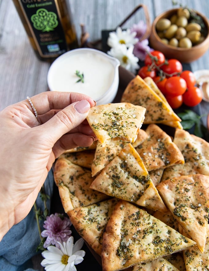 a hand holding a bitten piece of pita chips over the platter showing the texture