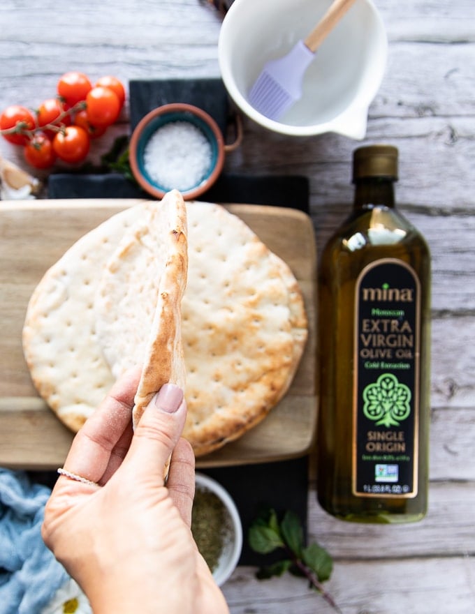 A hand holding the pita bread showing the side view thickness of the bread