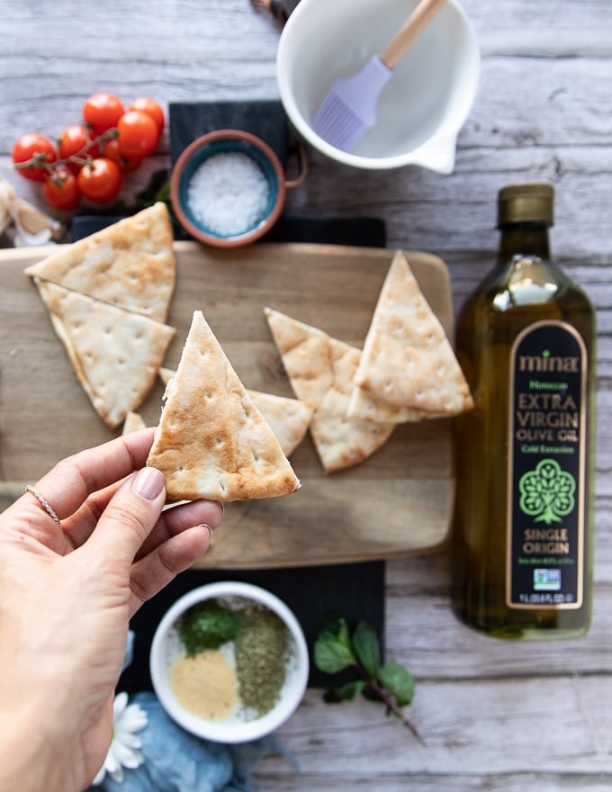 A hand holding a perfect slice of pita chip cut up from pita bread