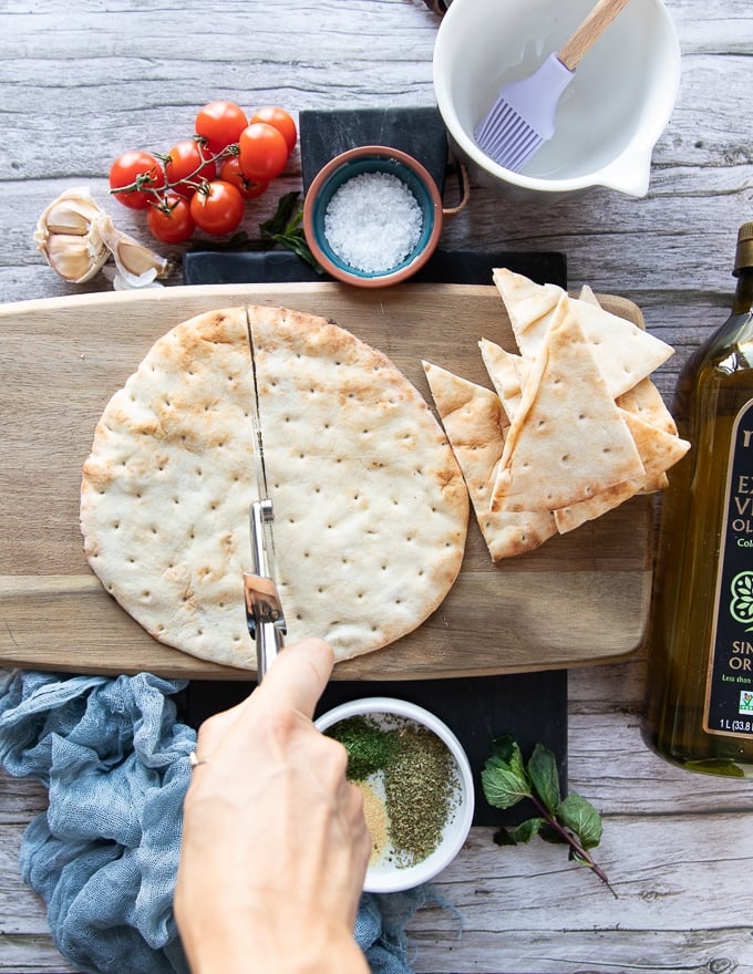 A hand holding a pizza cutter and slicing the pita bread in half first