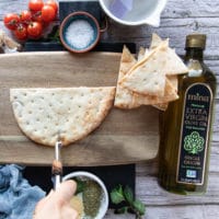 The pita hald bread on a cutting board and the hand holding a pizza slicer to slice the bread into quarters