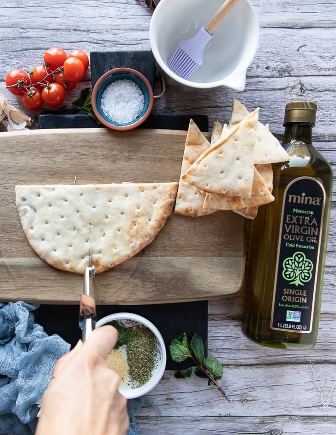 The pita hald bread on a cutting board and the hand holding a pizza slicer to slice the bread into quarters