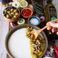 a hand pouring the feta dip in a plate and scooping the topping using a spoon