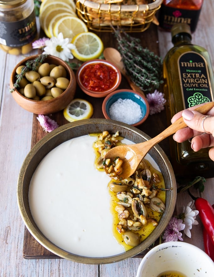 a hand pouring the feta dip in a plate and scooping the topping using a spoon