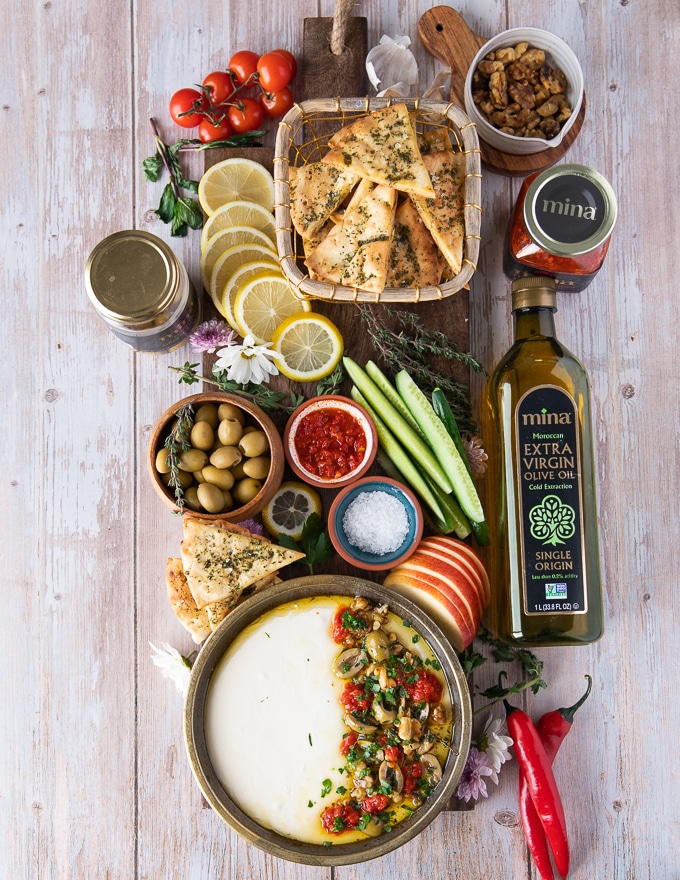 final board serving whipped feta including whipped feta on a plate with toppings and served along side pita chips, fresh apples, cucumbers and spicy harissa sauce