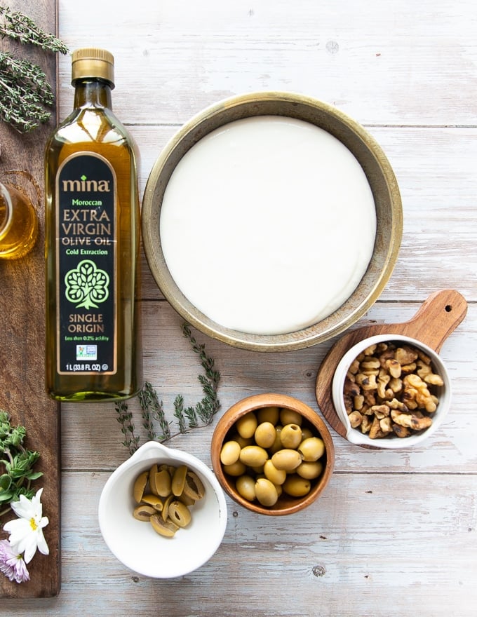 ingredients for topping the whipped feta incuding green olives, olive oil, walnuts and fresh thyme