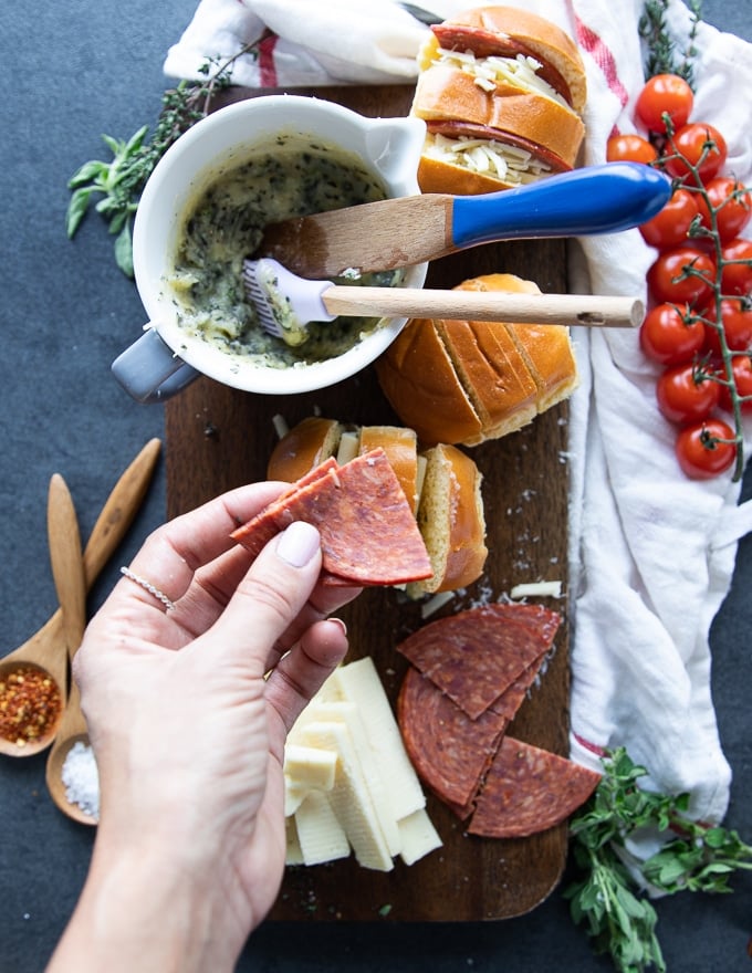 A hand holding a salami piece and ready to stuff it inside the air fryer pizza rolls