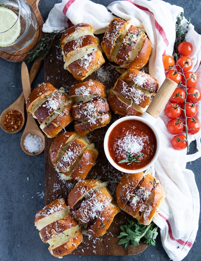 Air fryer pizza rolls on a wooden board surrounded by a bowl of pizza sauce and a white tea towel 