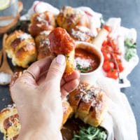 A hand holding a piece of air fryer pizza roll dipped in pizza sauce with melted cheese