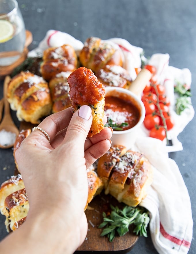 A hand holding a piece of air fryer pizza roll dipped in pizza sauce with melted cheese