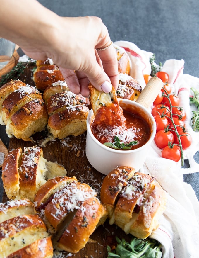 a hand dipping the air fryer pizza rolls in pizza sauce 