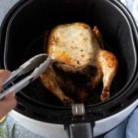 Flipped whole chicken in the air fryer basket with breast side up ready to continue cooking