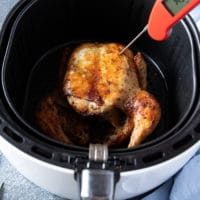 A meat thermometer placed in the middle of a whole chicken breast checking of the skin is done