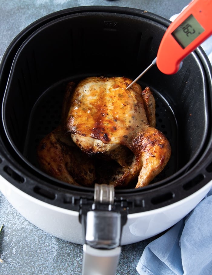 A meat thermometer placed in the middle of a whole chicken breast checking of the skin is done