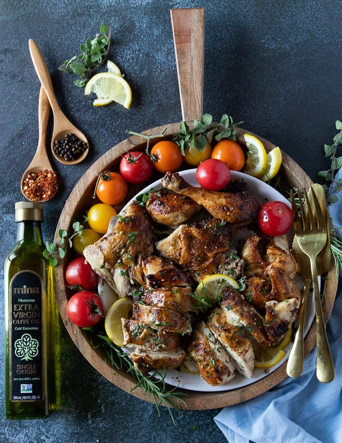 A plate of a whole air fryer roast chicken cut up and ready to serve with some fresh salad and extra chilli flakes for sprinkling, and olive oil for drizzling