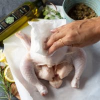 a hand patting down the whole hcicken with kitchen towels making sure it's dry