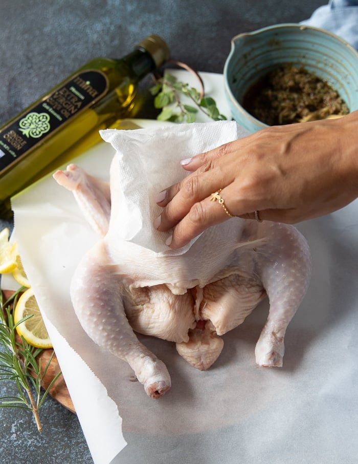 a hand patting down the whole hcicken with kitchen towels making sure it's dry