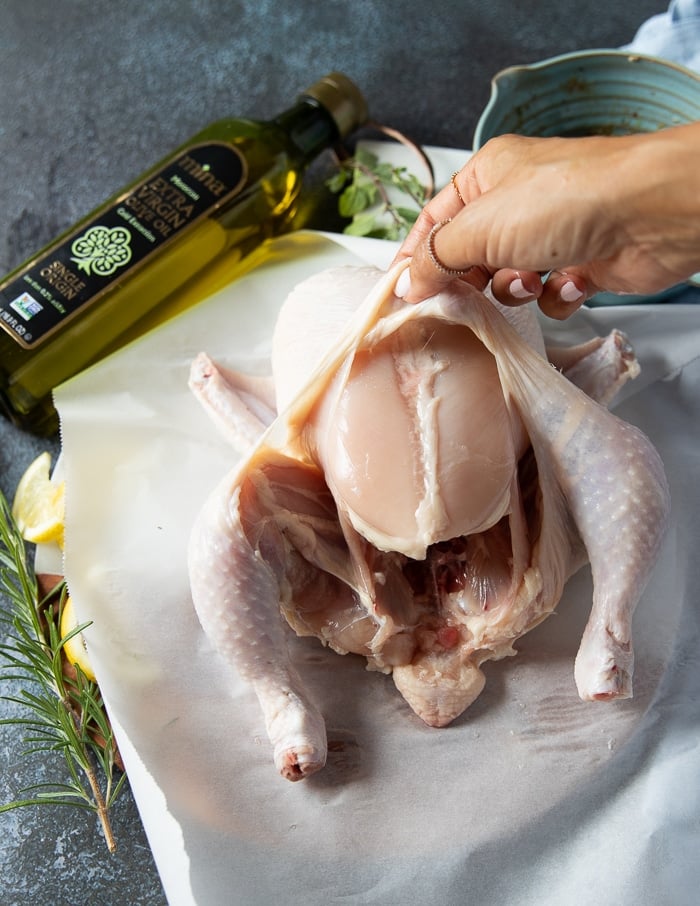 A hand separating the skin from the meat for a whole chicken to make sure it infuses with most flavor during air frying