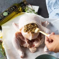 A spoon adding in the roast garlic and spice mixture between the skin and meat of the chicken