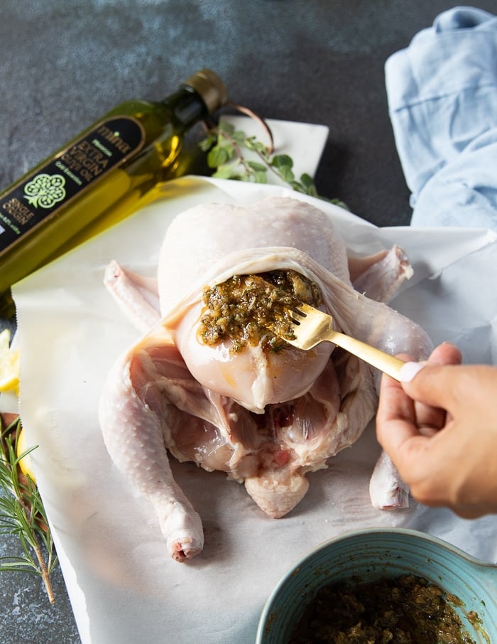 A spoon adding in the roast garlic and spice mixture between the skin and meat of the chicken