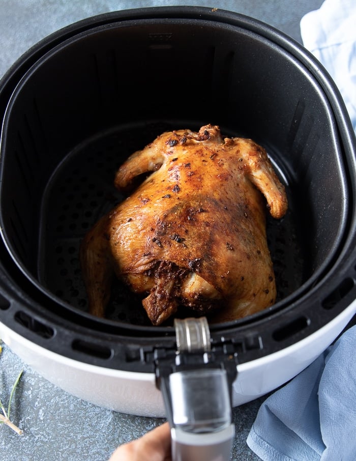 golden whole chicken in the air fryer after cooking half way, ready to be flipped to continue air frying