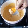 A hand dipping in the tortilla into the pot to check if the sauce is ready