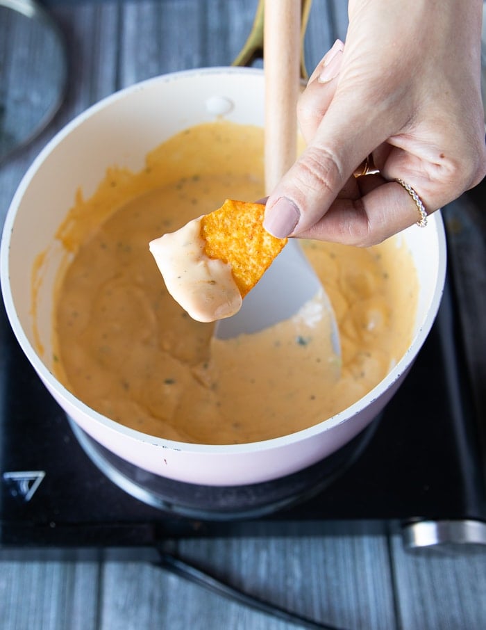 A hand dipping in the tortilla into the pot to check if the sauce is ready