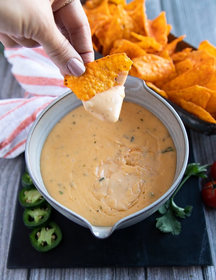 a hand holding a piece of chips dipped in cheese sauce showing how saucy it is