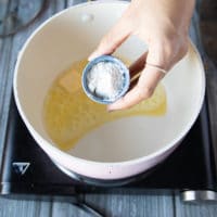 A hand pouring in the flour into the pot of butter