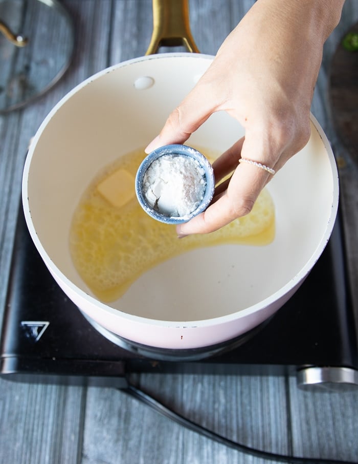 A hand pouring in the flour into the pot of butter