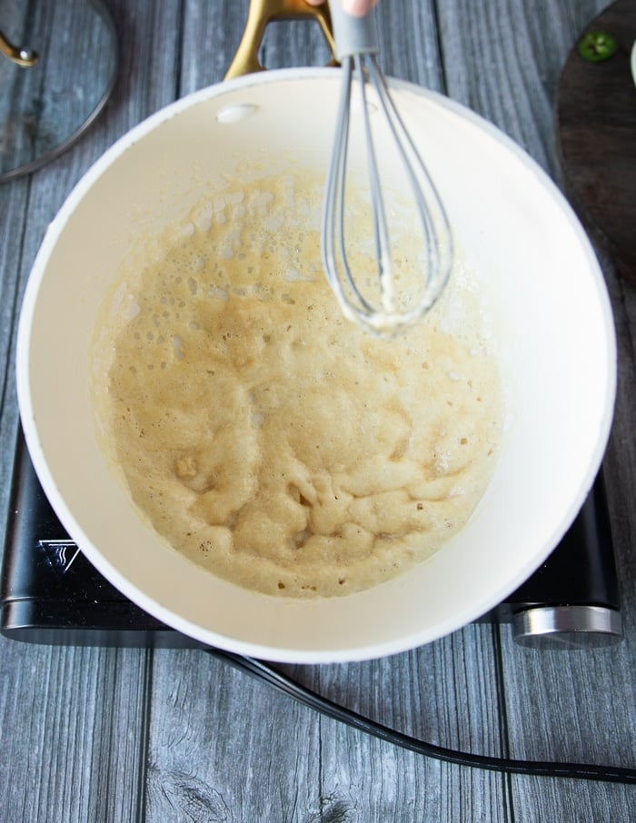 A whisk whisking in the flour into the butter to make the roux base of the sauce