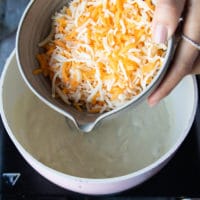 A hand pouring in the cheese into the post gradually