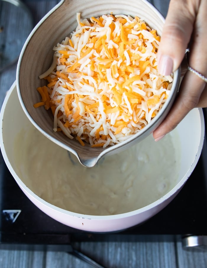 A hand pouring in the cheese into the post gradually