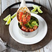 a spoon adding in a layer of tuna tartare over the avocado layer